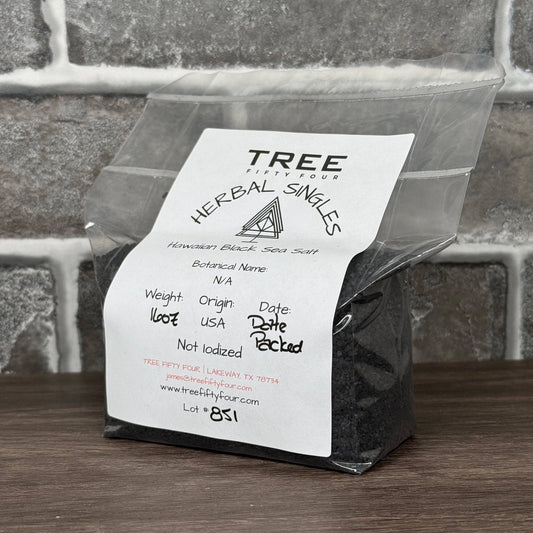 Hawaiian black sea salt in clear resealable bag with white label on wooden surface against gray brick background
